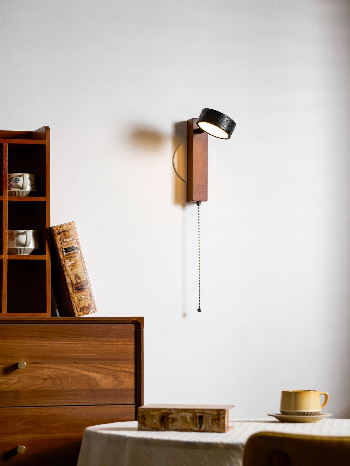 Swivelling back toward the viewer, this Clérachic wall light hangs above a round table holding a book and teacup.