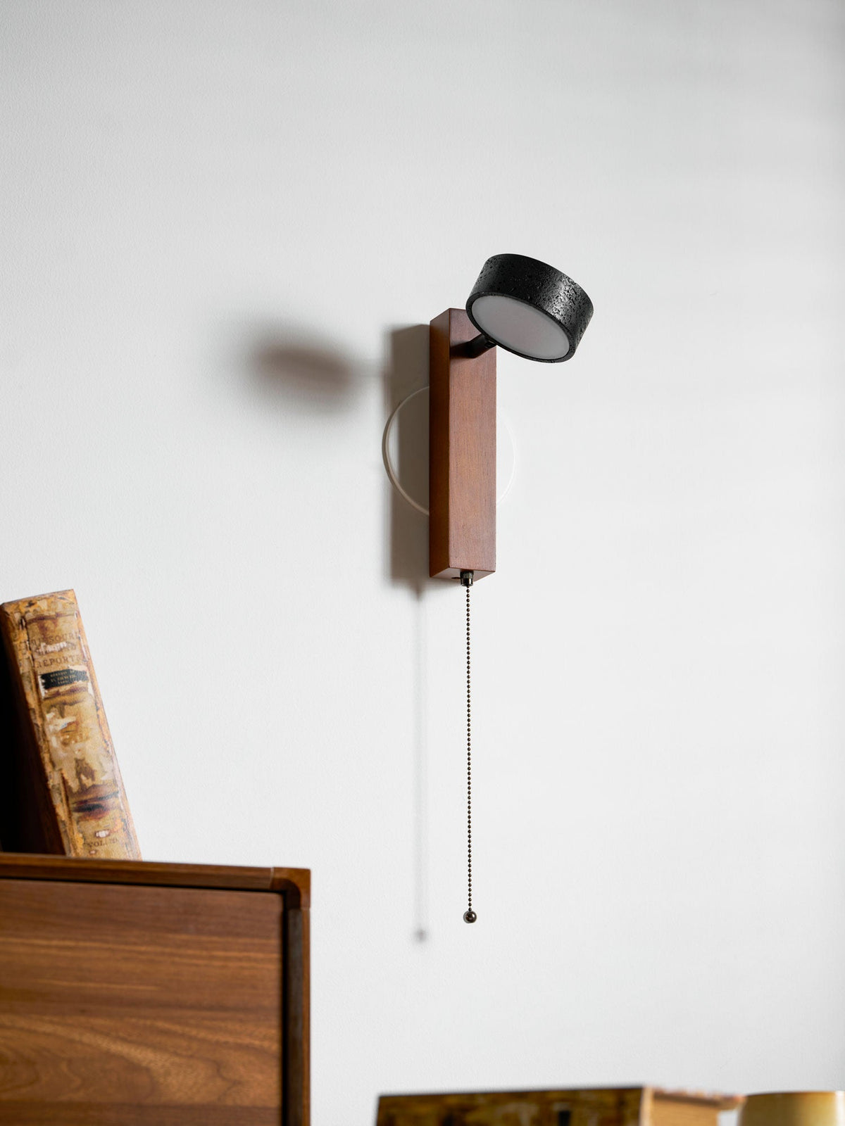 Pivoted to the left, this Clérachic wall light hangs beside a bookcase holding cups and books.