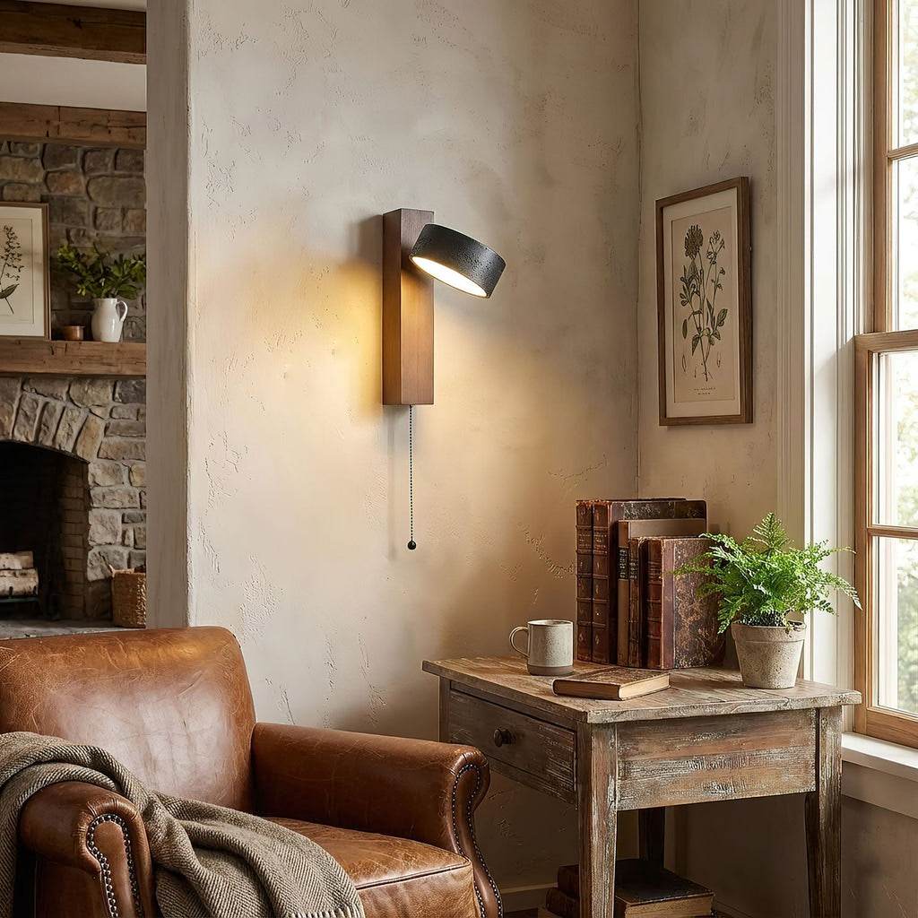 Beside a stone fireplace, this Clérachic wall light glows warm above a table holding books and a fern.