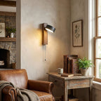 Beside a stone fireplace, this Clérachic wall light glows warm above a table holding books and a fern.