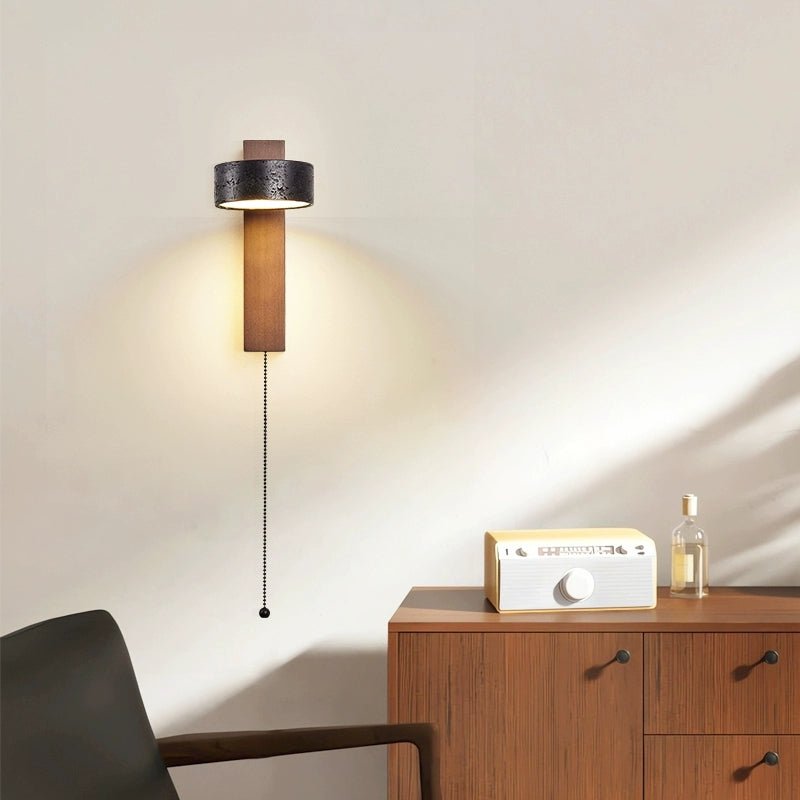 A credenza with a radio and bottle sits beneath this Clérachic wall light, its pull chain hanging warm-lit against the wall.