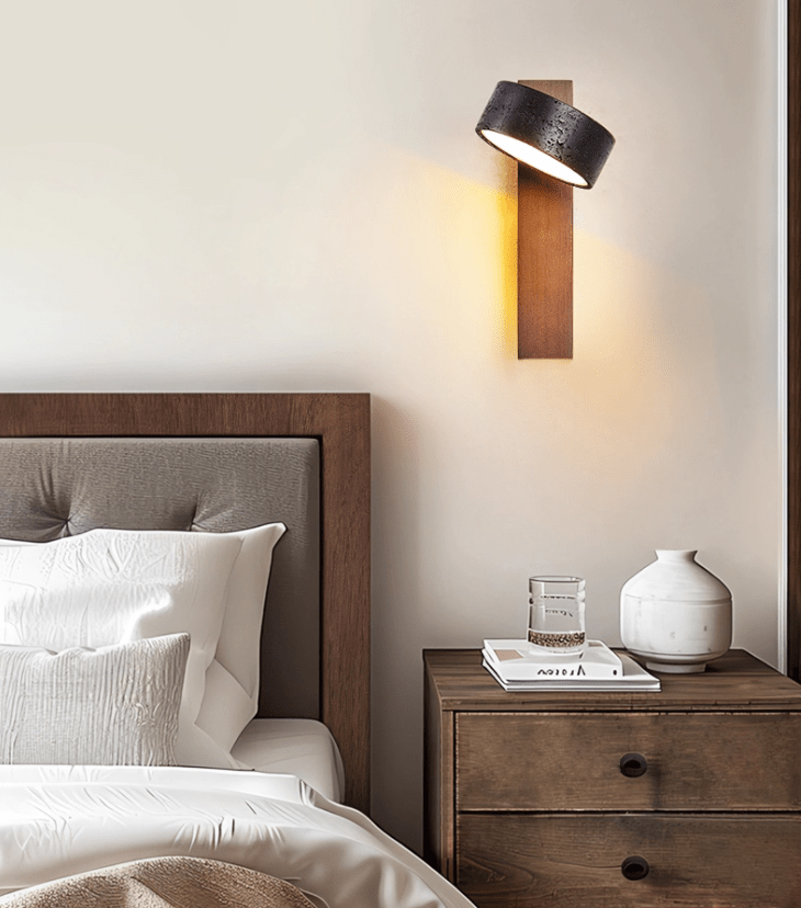 A linen headboard, a vase and a book on the nightstand sit beneath this Clérachic wall light.