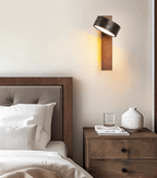 A linen headboard, a vase and a book on the nightstand sit beneath this Clérachic wall light.