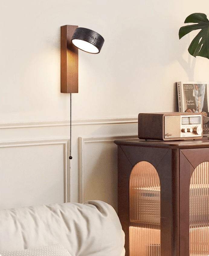 Beside a wood cabinet holding a vintage radio, this Clérachic wall light glows warm with its pull chain hanging down.
