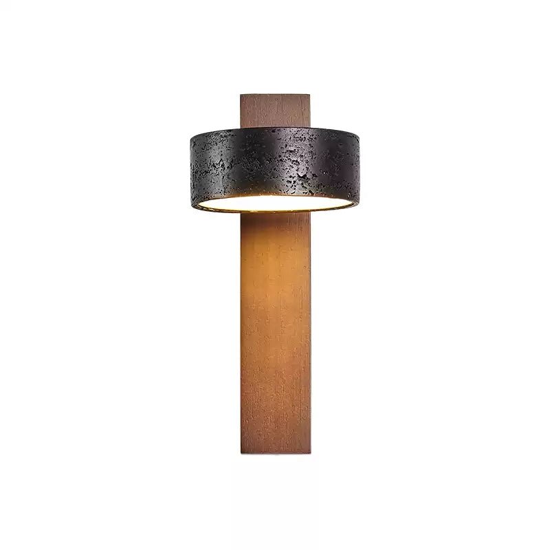 Front view of this Clérachic wall light on white, warm light glowing inside its black travertine drum shade.