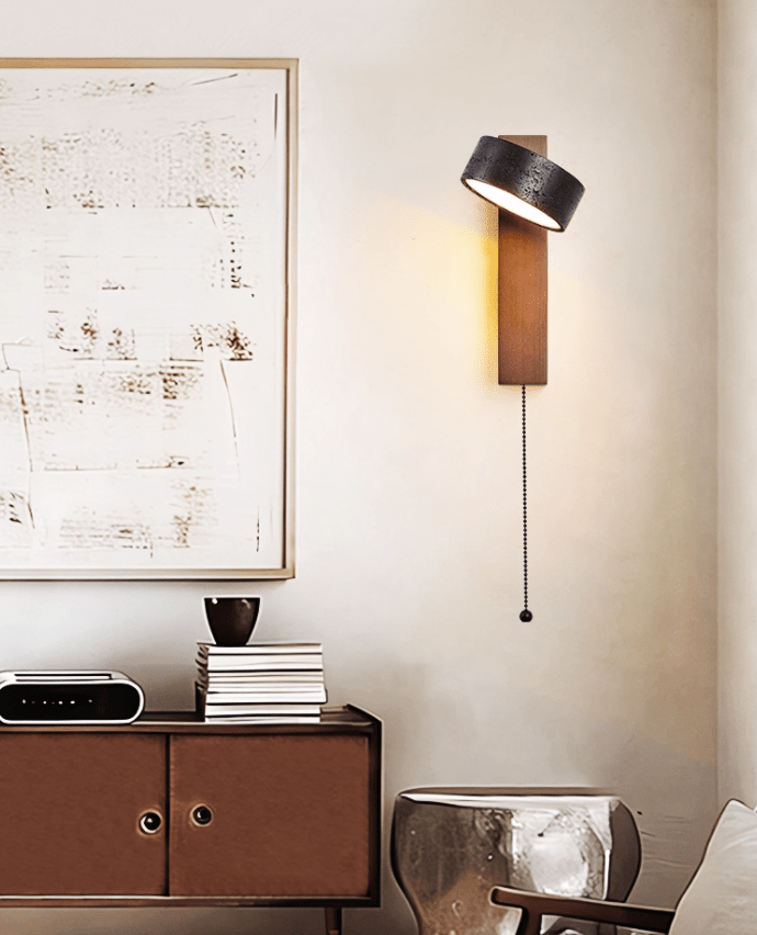 An abstract painting and a sideboard with books and a small sculpture sit beneath this Clérachic wall light.