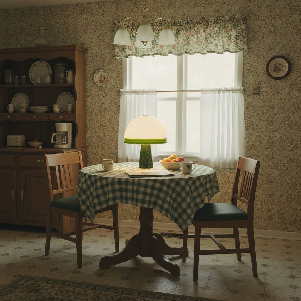 Warm light spills from the Clérachic dome table lamp on a hutch beside a breakfast table laid with a green checked tablecloth.