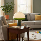 Clérachic dome table lamp lit on a wooden side table beside a beige sofa, with yellow cushions and a potted plant nearby.
