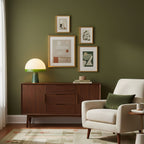 Beneath a gallery wall of framed prints, the Clérachic dome table lamp lights a wooden credenza beside a cream armchair.
