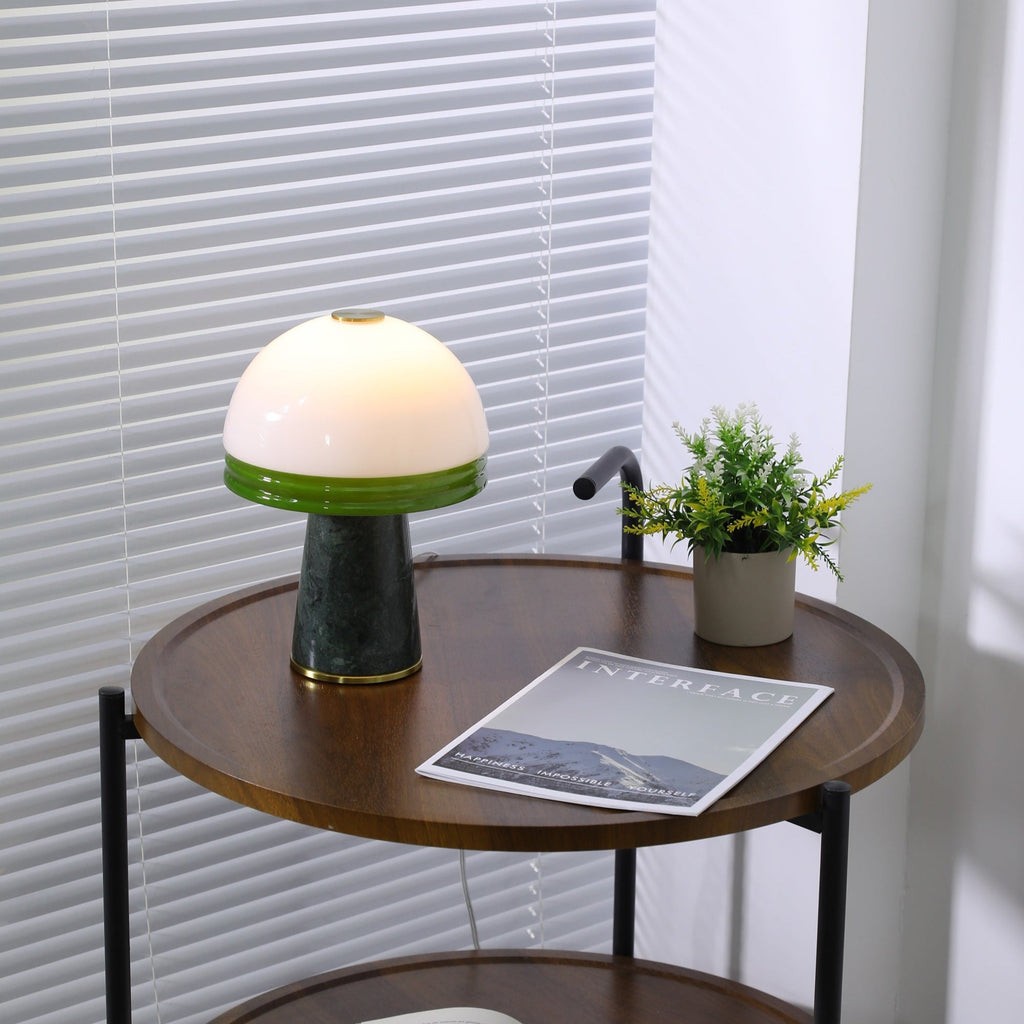 A full view of the lit Clérachic table lamp on the round table, with its plant, magazine and cord all visible.