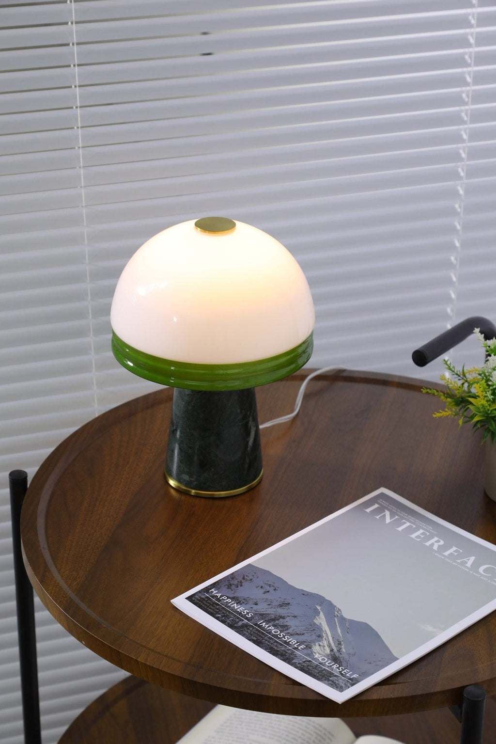 Zoomed out, the Clérachic table lamp stands on a two-tier round table with a folded throw on the shelf below.