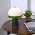 A Clérachic table lamp lit beside a small potted plant, its green rim bright against the round tabletop.