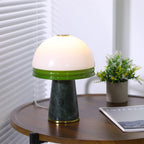 A tighter crop of the Clérachic dome lamp beside the potted plant, green glass rim glowing warmly.