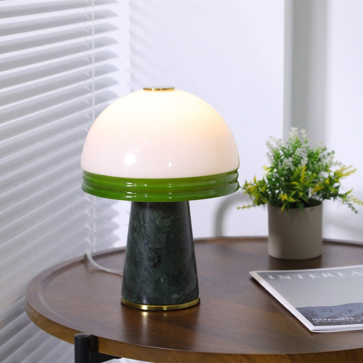 A tighter crop of the Clérachic dome lamp beside the potted plant, green glass rim glowing warmly.