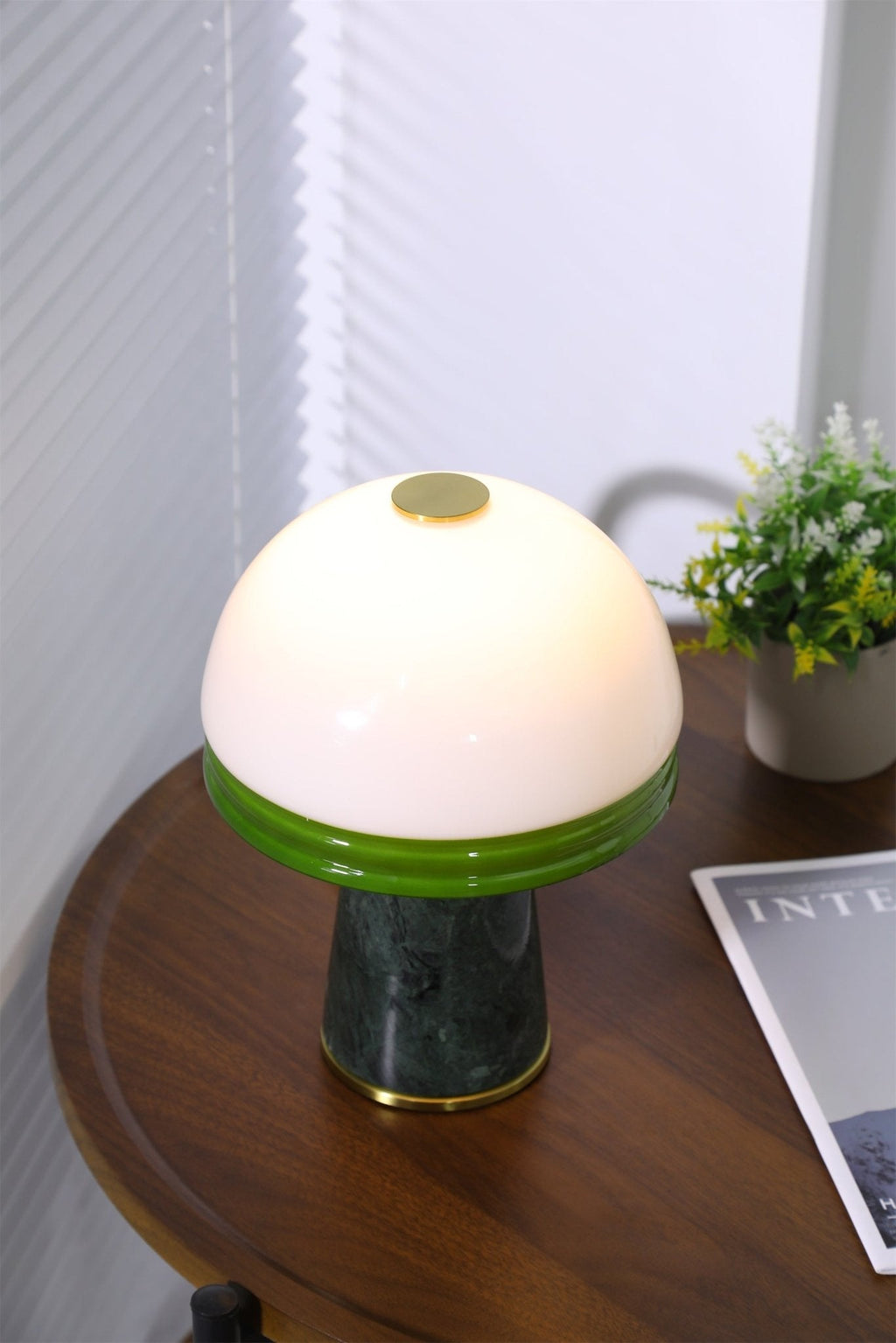 A narrow, close crop of the lit Clérachic table lamp's dome, with the potted plant just visible at the edge.