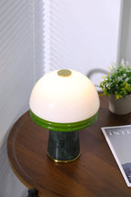 A narrow, close crop of the lit Clérachic table lamp's dome, with the potted plant just visible at the edge.