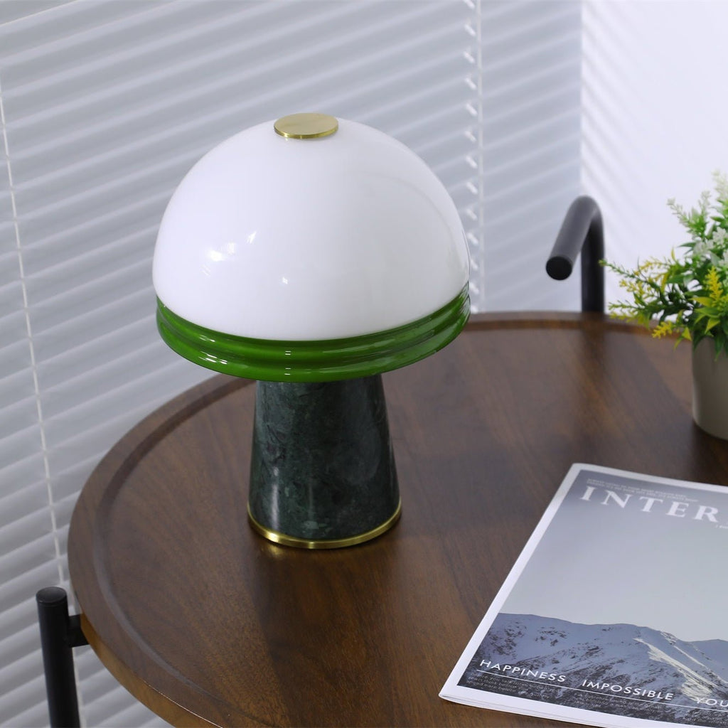 The Clérachic table lamp glows on the round table, a potted plant in the corner and its cord visible left.