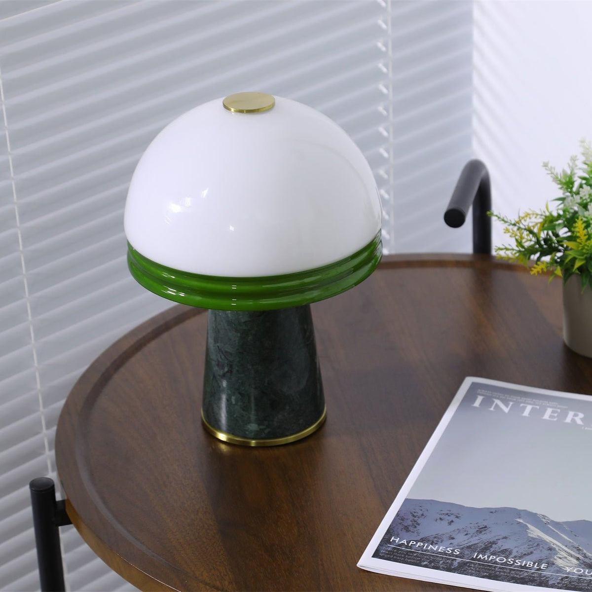 The Clérachic table lamp glows on the round table, a potted plant in the corner and its cord visible left.