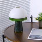 The lit Clérachic table lamp sits on the round table, a plant to its right and a magazine partly cropped.