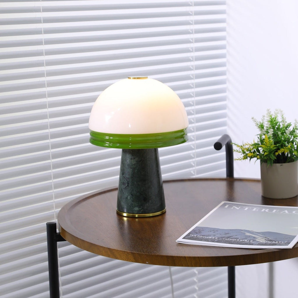 A closer crop of the Clérachic dome lamp lit on the round table, the green glass rim catching the light.