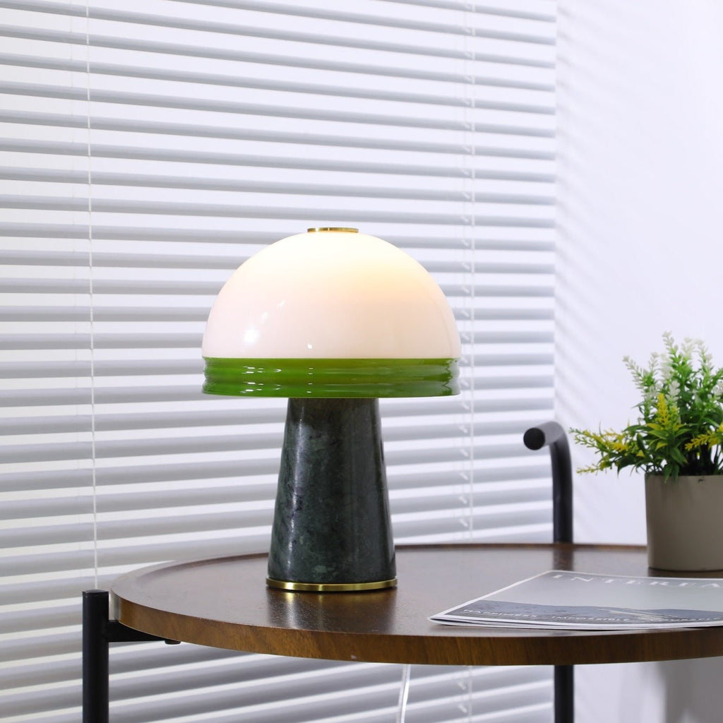 A tighter, centred crop of the lit Clérachic table lamp on the round wooden table against the blinds.