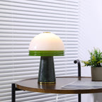 A tighter, centred crop of the lit Clérachic table lamp on the round wooden table against the blinds.