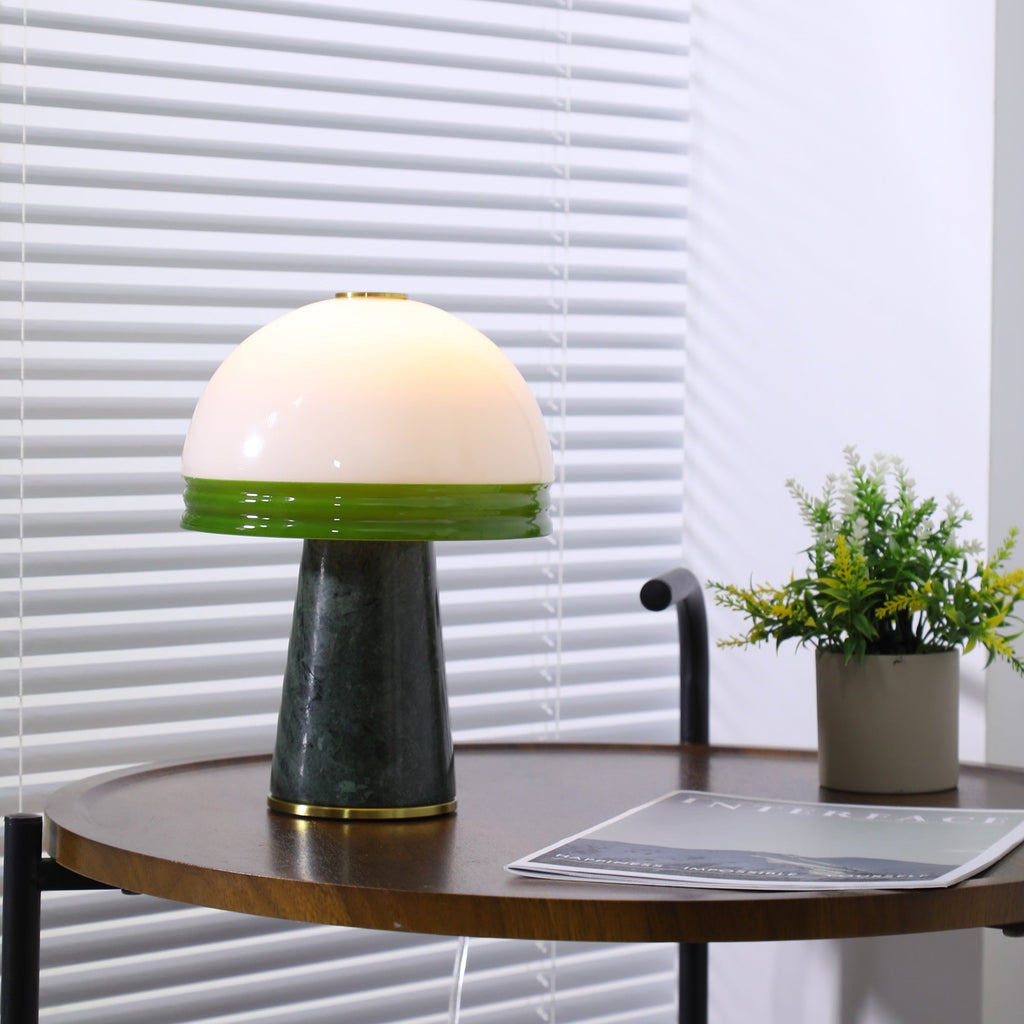 The lit Clérachic table lamp sits beside a potted plant on the round table, its magazine just in frame.