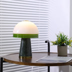 The lit Clérachic table lamp sits beside a potted plant on the round table, its magazine just in frame.