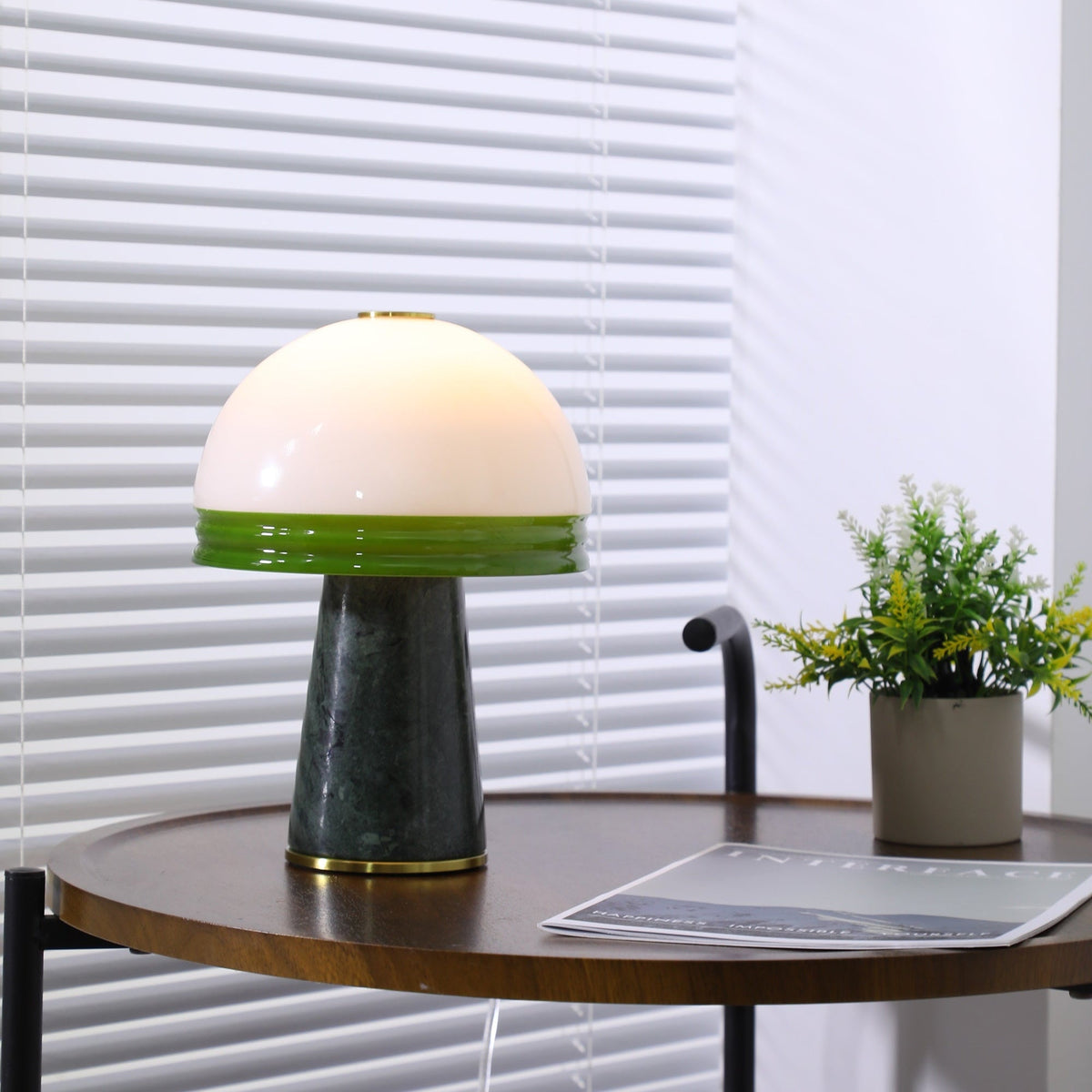 The lit Clérachic table lamp sits beside a potted plant on the round table, its magazine just in frame.