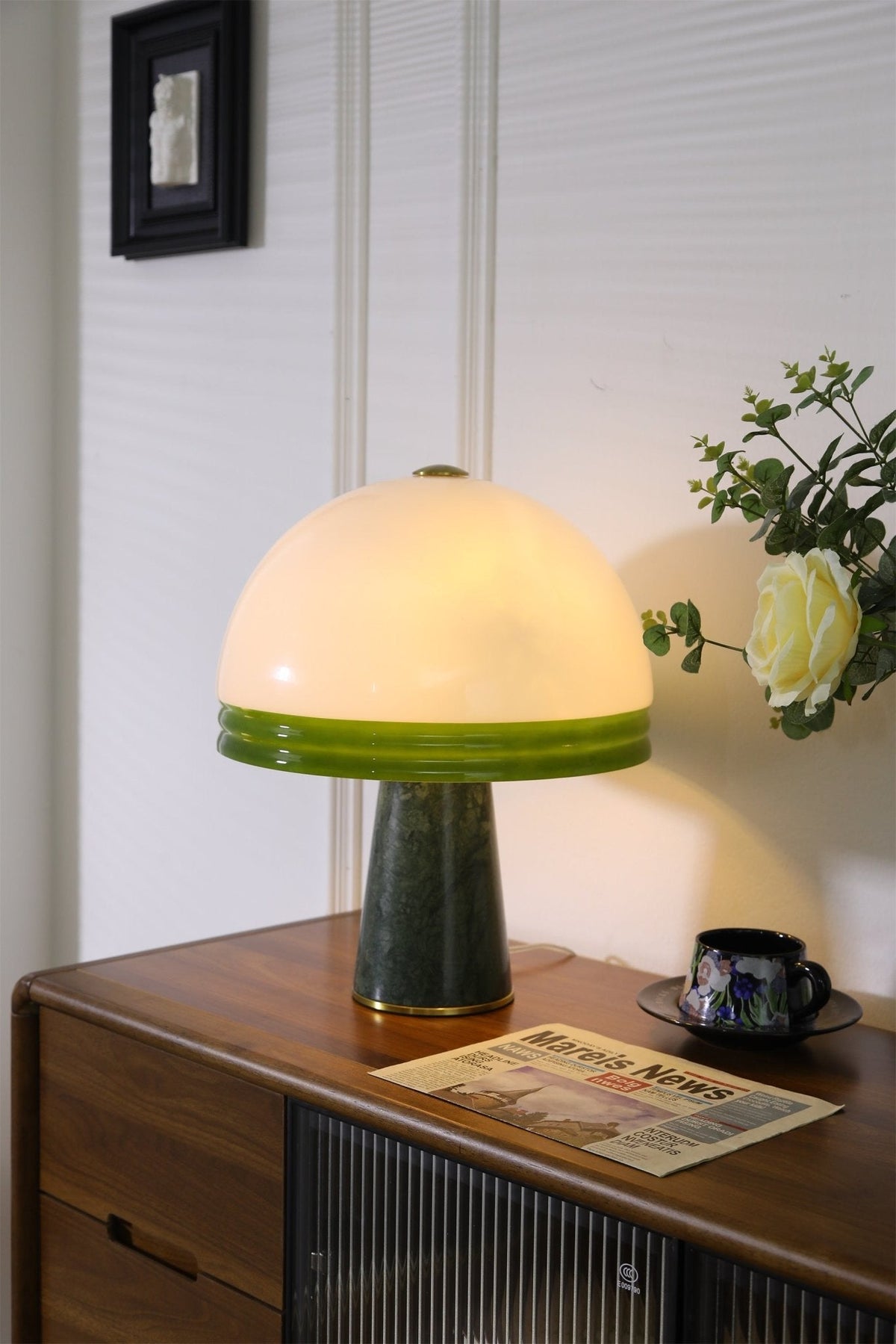 Near a window, the Clérachic dome table lamp glows on a nightstand beside a small vase of flowers and a folded newspaper.
