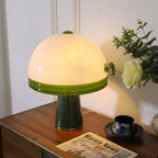 Clérachic dome table lamp lit close-up, a cream rose brushing the edge of the frame beside the glowing shade.