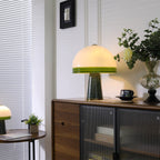 Near a window with blinds, the Clérachic dome table lamp lights a sideboard beside a small round table and potted plant.