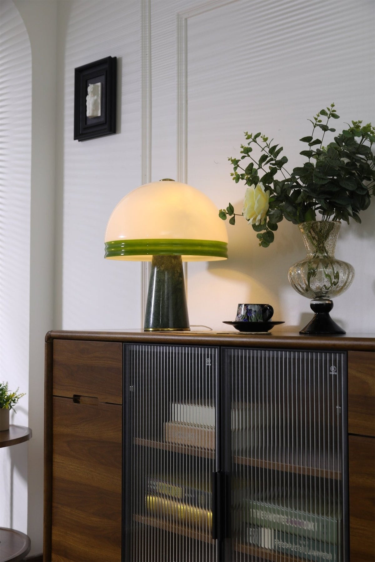 A black-framed picture hangs above the sideboard where the Clérachic dome table lamp glows beside a rose in a glass vase.