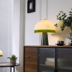 Clérachic dome table lamp glowing beside a window with blinds, a round table and small potted plant in the foreground.