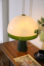 Clérachic dome table lamp lit close to a cream rose, a glass vase visible at the right edge of the frame.