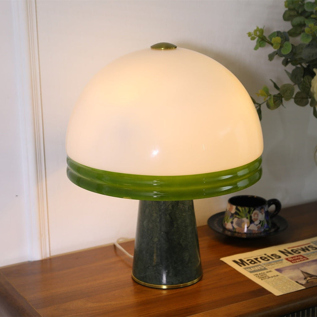Close-up of the lit Clérachic dome table lamp with its glass dome filling most of the frame beside eucalyptus stems.