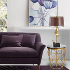 In a styled living room, the Clérachic gold spiral lamp sits on a small glass-and-gold table beside a purple velvet sofa.