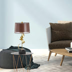 A teal pouf and woven armchair share this pale blue room with the Clérachic gold spiral lamp on its round glass table.