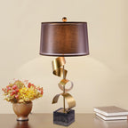 Dried flowers and stacked books share the wooden table with the Clérachic gold spiral lamp, a warm beige wall behind.