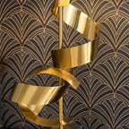 Close-up of the Clérachic gold spiral stem against dark art-deco wallpaper, showing the ribbon's brushed metal finish.
