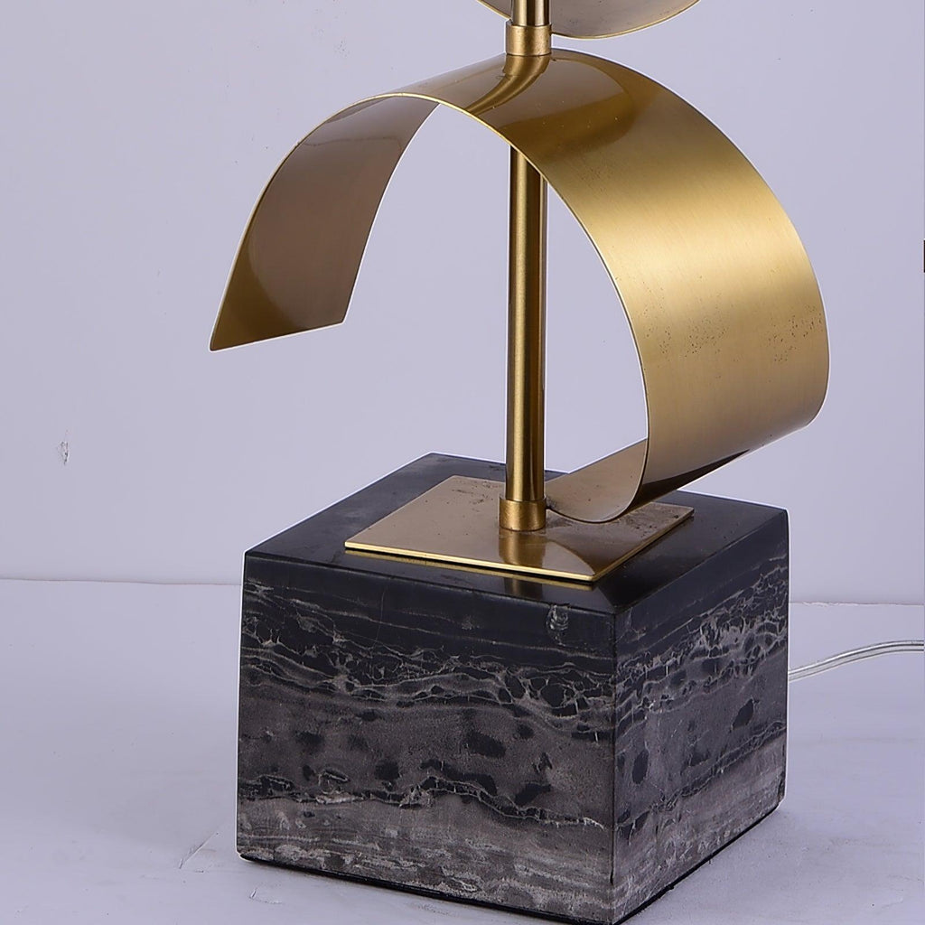 Close-up of the Clérachic lamp's gold spiral base seated on its black marble cube, cord visible on a white surface.