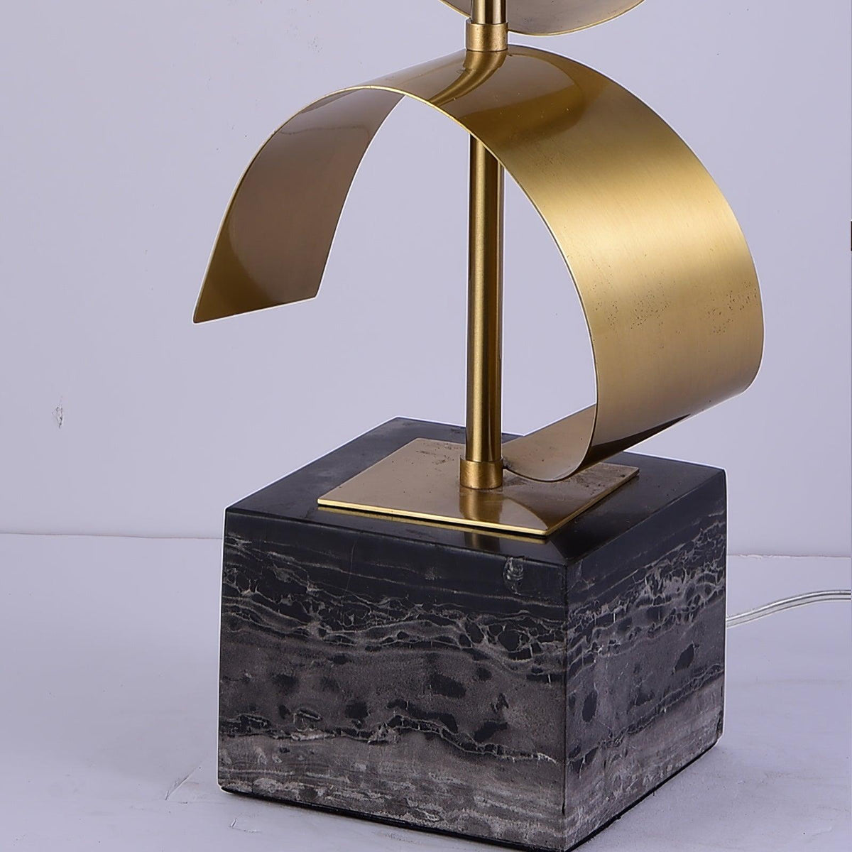 Close-up of the Clérachic lamp's gold spiral base seated on its black marble cube, cord visible on a white surface.