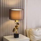 Clérachic gold spiral table lamp lit on a white bedside nightstand, its warm glow softening the fluted wall panelling.