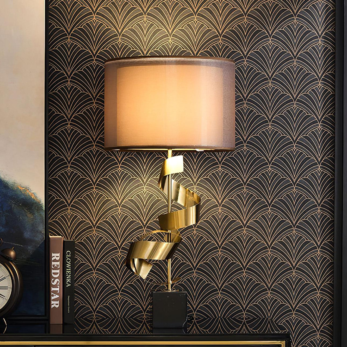 Clérachic gold spiral table lamp on a black shelf against art-deco wallpaper, standing beside a vintage clock and books.