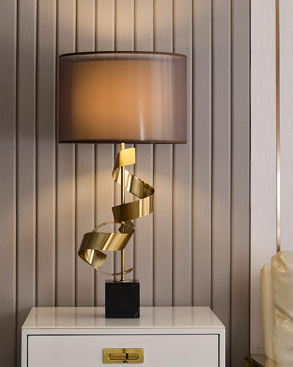 Clérachic gold spiral table lamp glowing on a white nightstand, cropped close to show the coiled brass stem and shade base.