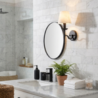 In a marble-tiled bathroom, this black Clérachic sconce lights the wall beside a round mirror.