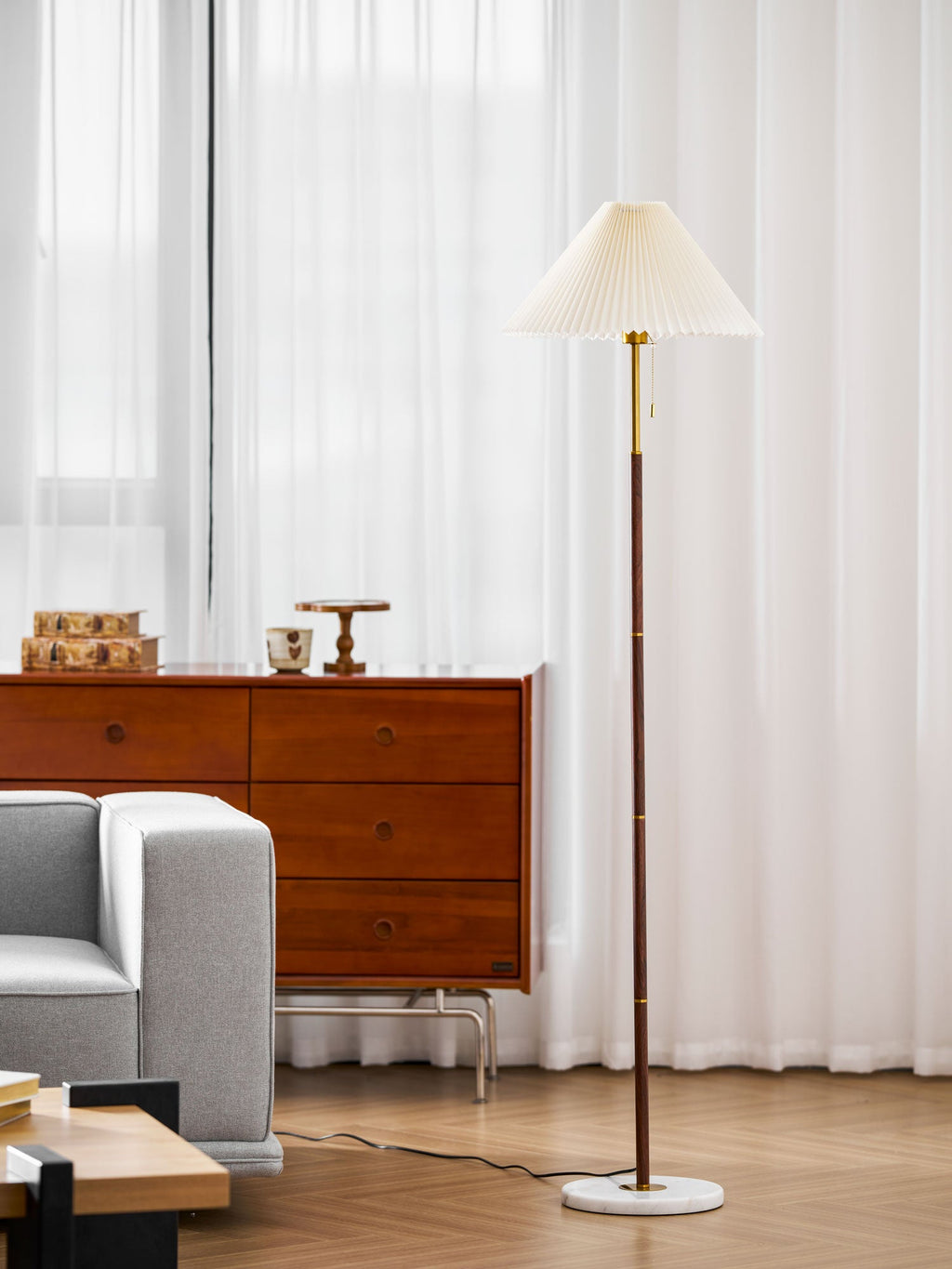 Clérachic floor lamp beside a dark wood sideboard holding small ceramics, sheer curtains framing the window behind it.