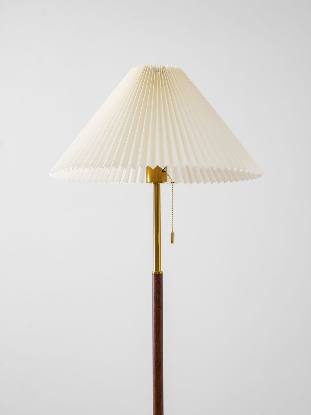 Angled close-up beneath the Clérachic floor lamp's pleated shade, showing the brass gallery, pull-chain and walnut pole.