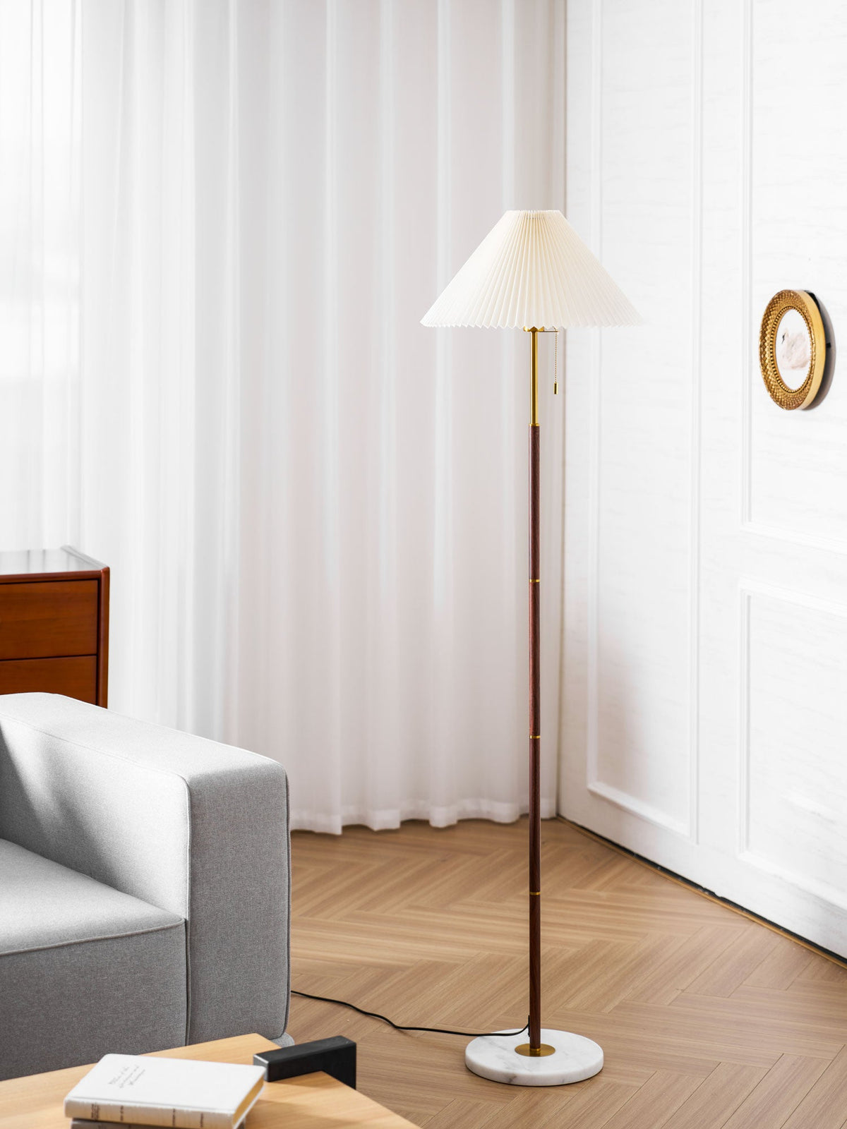 Clérachic pleated-shade floor lamp in a room corner, with a stack of books on the floor beside its marble base.