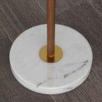 Close-up of the Clérachic floor lamp's round white marble base, where a brass collar meets the walnut pole.